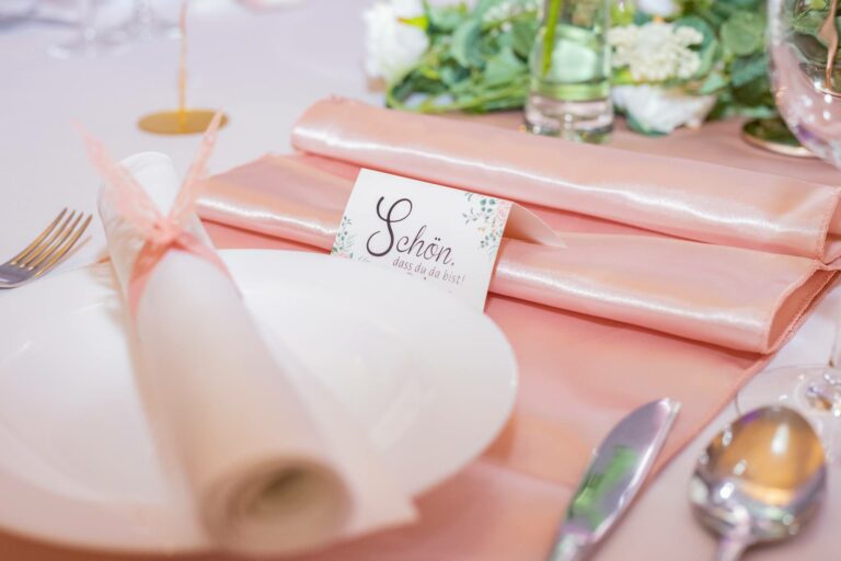 Gedeckter Platz mit Namenskarte und rosa Serviette auf einer Hochzeitstafel – Metadrom Eventcenter Großefehn