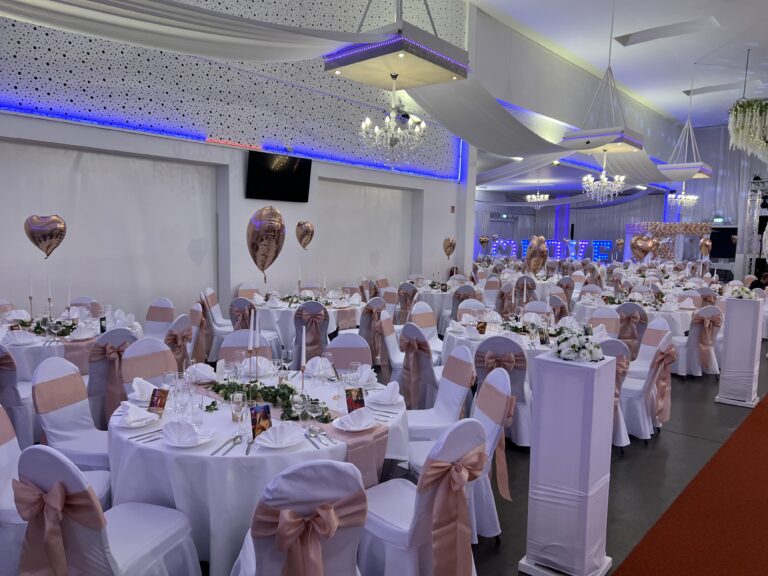 Großer Hochzeitssaal mit runden Tischen und Stuhlschleifen – Metadrom Eventcenter Großefehn