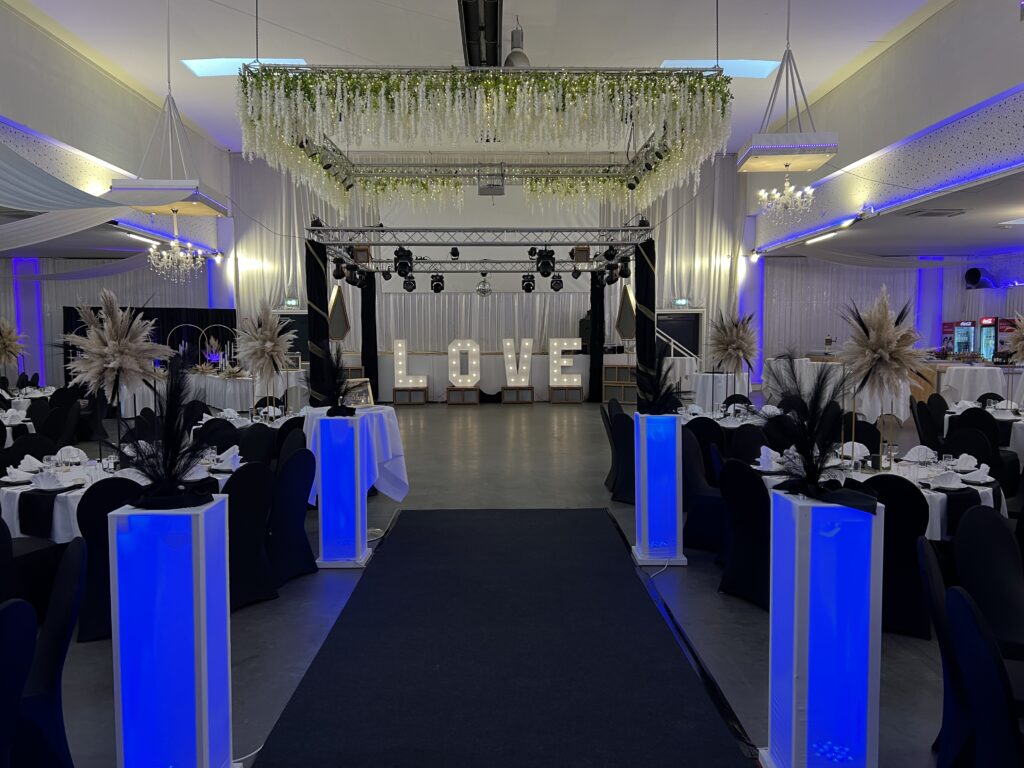 Dunkel eingedeckte Tische mit blau beleuchteten Säulen und Leuchtbuchstaben LOVE – Metadrom Eventcenter Großefehn