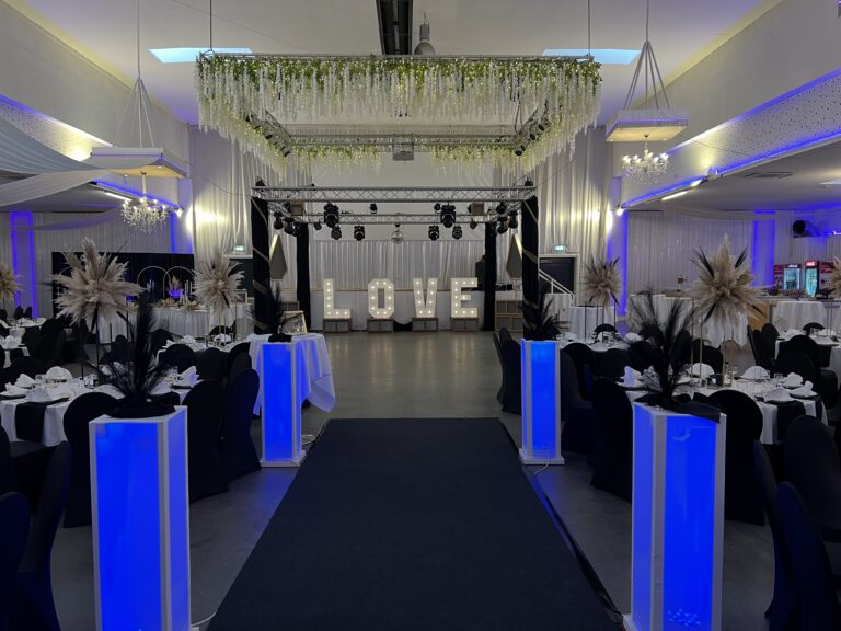 Dunkel eingedeckte Tische mit blau beleuchteten Säulen und Leuchtbuchstaben LOVE – Metadrom Eventcenter Großefehn