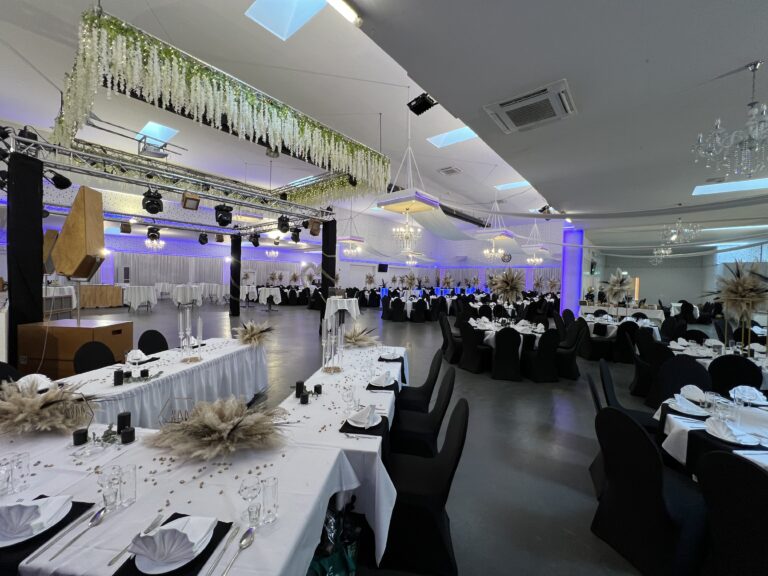 Hochzeitssaal mit schwarz-weißer Tischdekoration und Blütendecke – Metadrom Eventcenter Großefehn