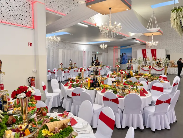 Hochzeitsbuffet an runden Tischen mit roten Schleifen und Kronleuchtern – Metadrom Eventcenter Großefehn