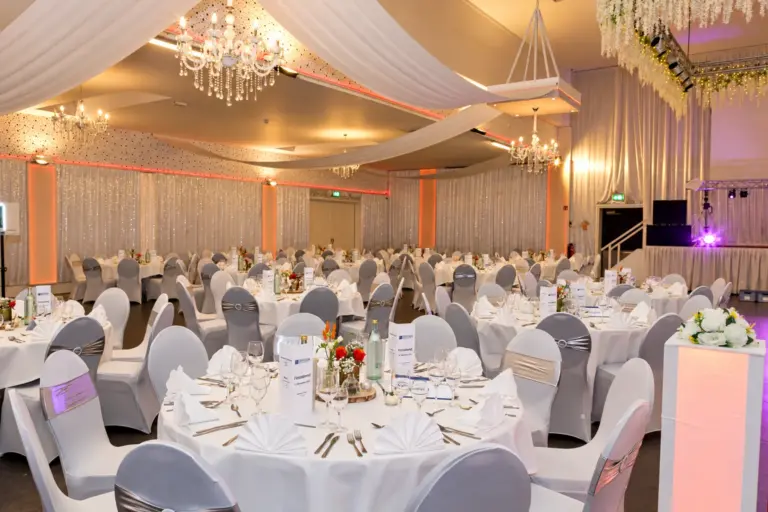 Festsaal mit Deckentüchern, Kronleuchtern und runden Tischen – Metadrom Eventcenter Großefehn