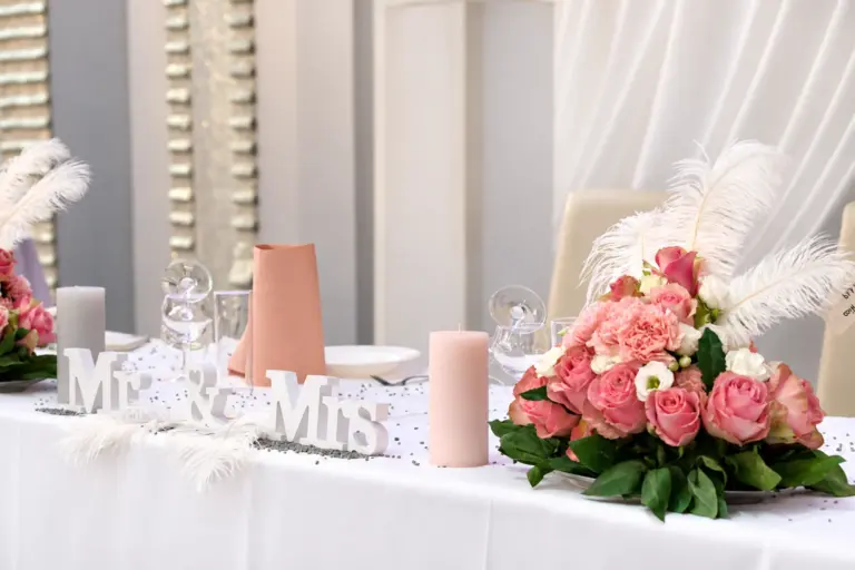 Brauttisch mit „Mr & Mrs“-Schriftzug, Rosen und Federn – Metadrom Eventcenter Großefehn